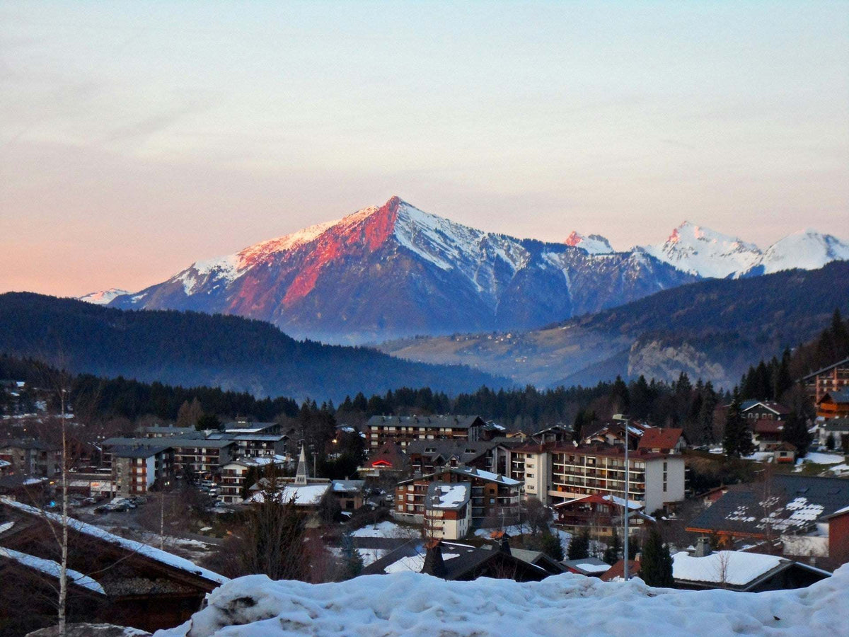 Colorado mountain town with snow-dusted rooftops beneath rugged, snow-capped peaks at sunset; The Best Mountain Towns feature.