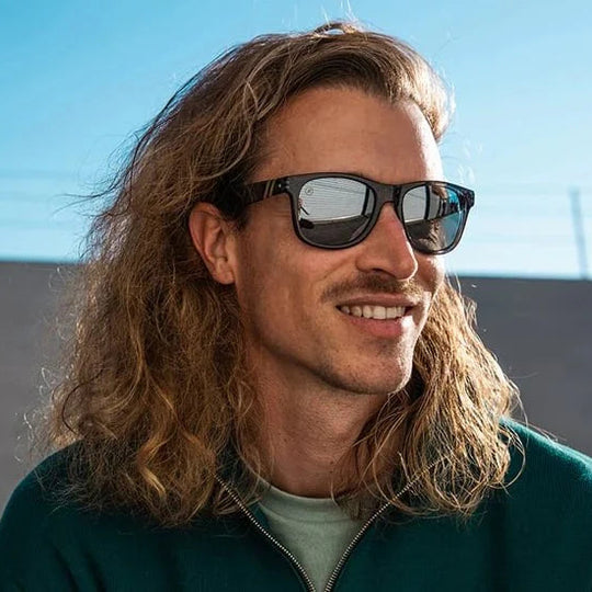 Man with long hair wearing sunglasses against a blue sky background