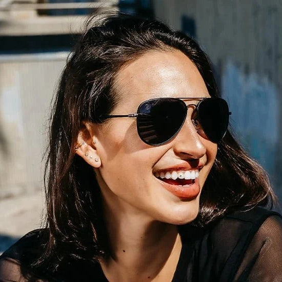 Woman wearing sunglasses smiling outdoors with a textured wall in the background