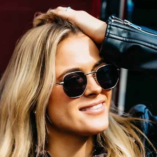 Woman wearing sunglasses and a black leather jacket in front of a red car.