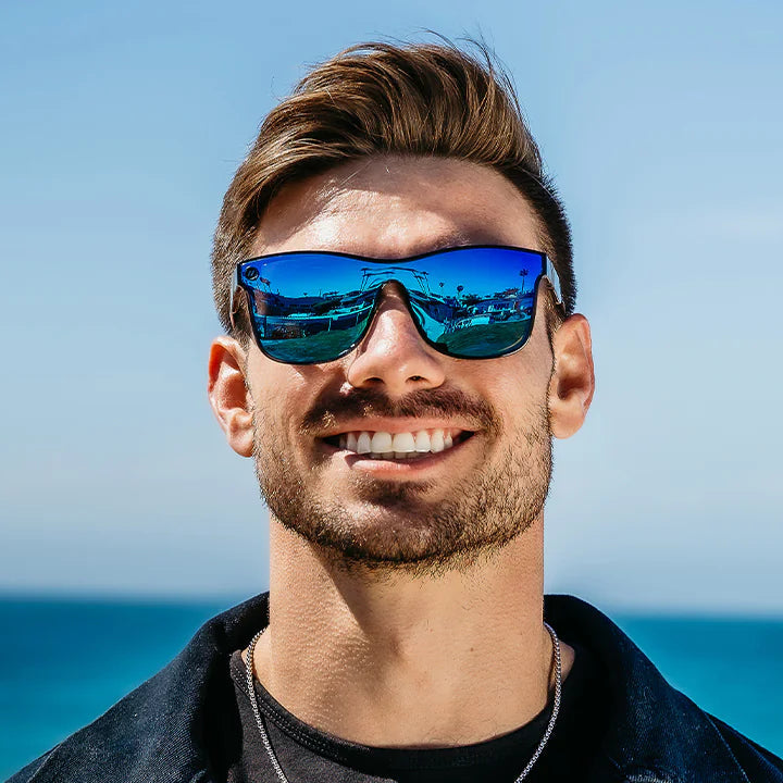 Man wearing blue reflective sunglasses with a clear blue sky and ocean background