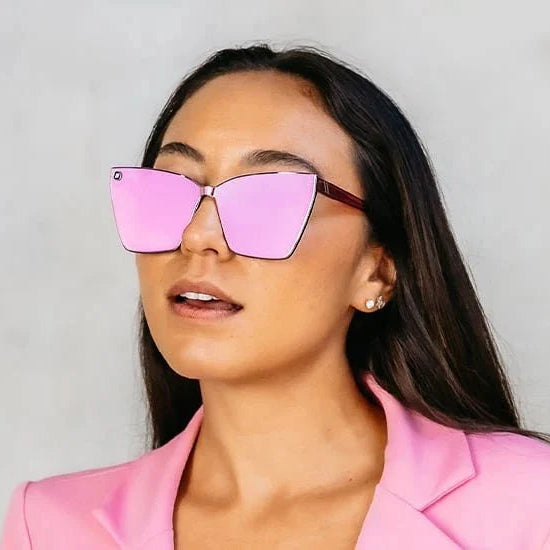 Woman wearing pink sunglasses and a pink blazer against a gray background