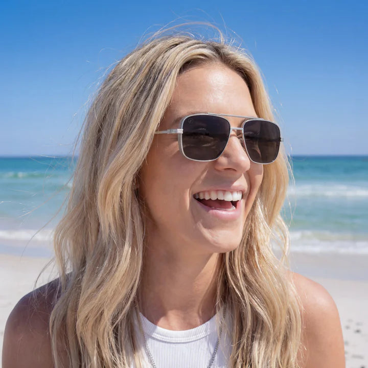 Woman wearing sunglasses on a beach with clear blue sky and ocean.