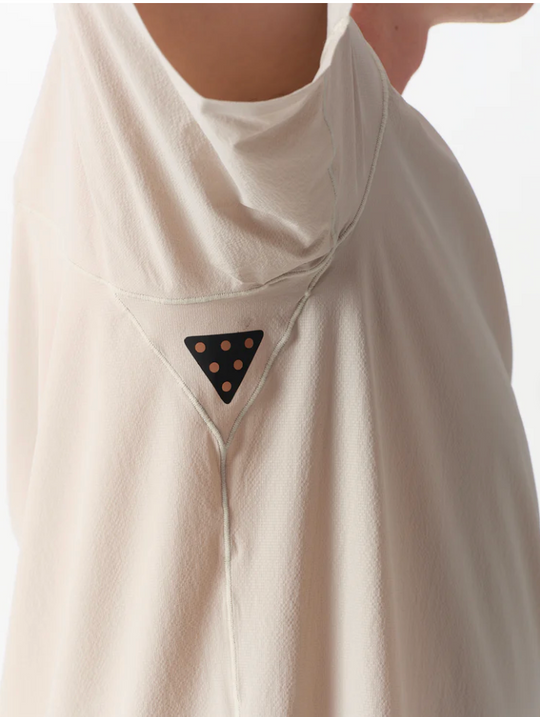 Close-up of a person wearing a draped, high-neck cream-colored garment with a small black triangular patch featuring gold dots near the chest.
