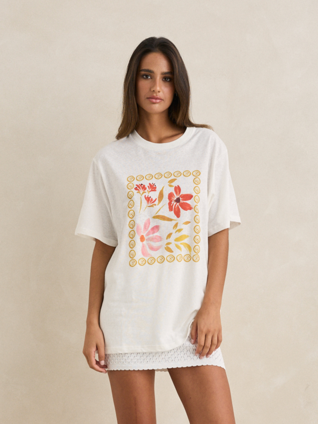Woman wearing a white t-shirt with floral designs on a beige background